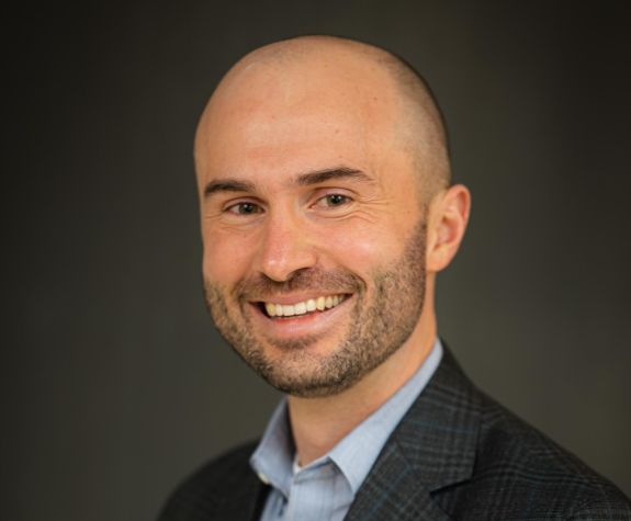 A portrait of a man wearing a suit in front of a gray background