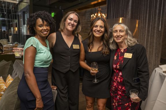 Four individuals dressed in business attire in an indoor setting smiling at the camera