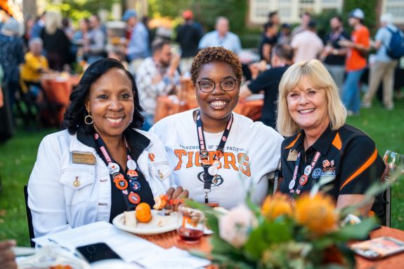 Three alumni sit at an outdoor event.