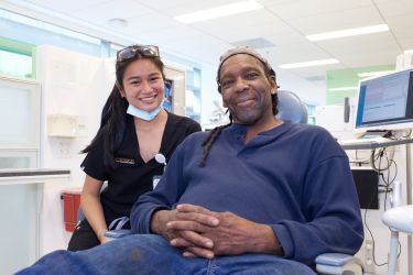 Woman dentist at the side of a dental chair with male black patient