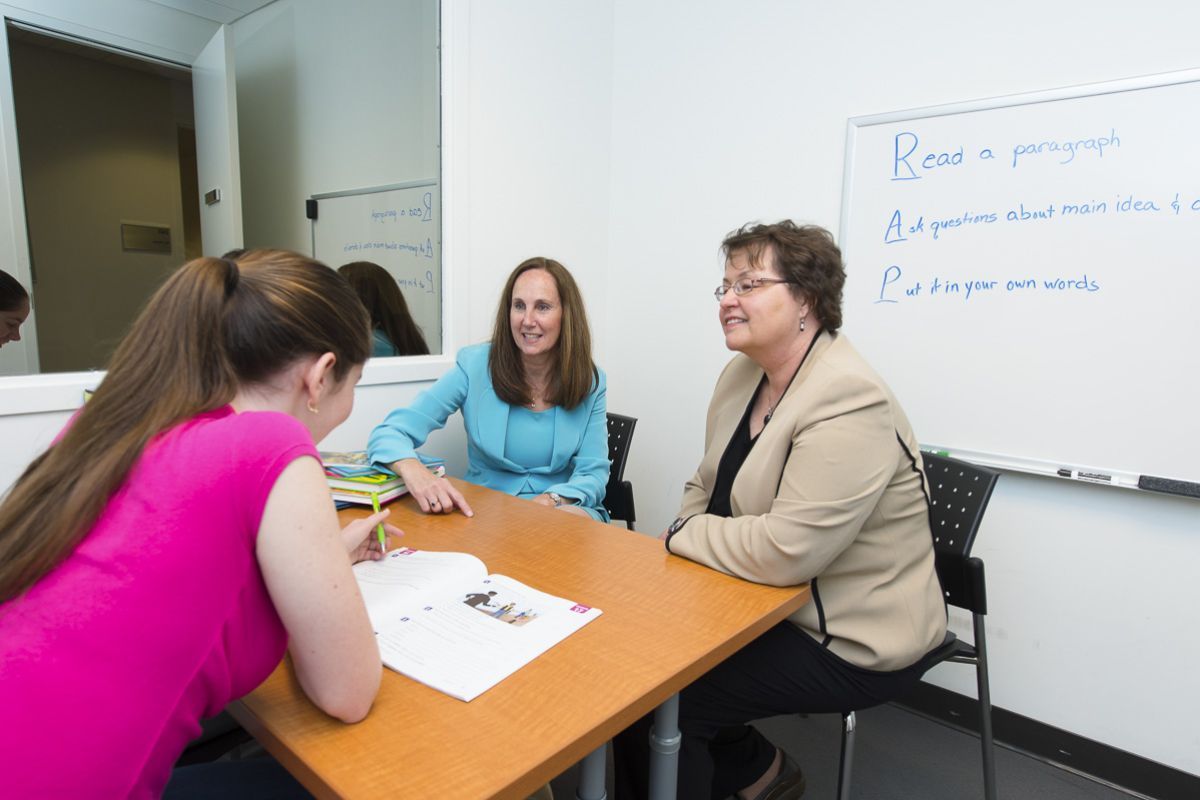 Image shows two Speech-Language Pathology faculty members sitting across a table from a student. 
