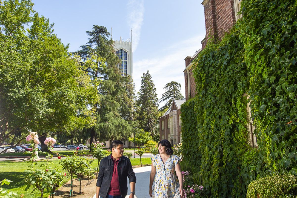 male student with cello case and female student walking under brick arch covered with ivy