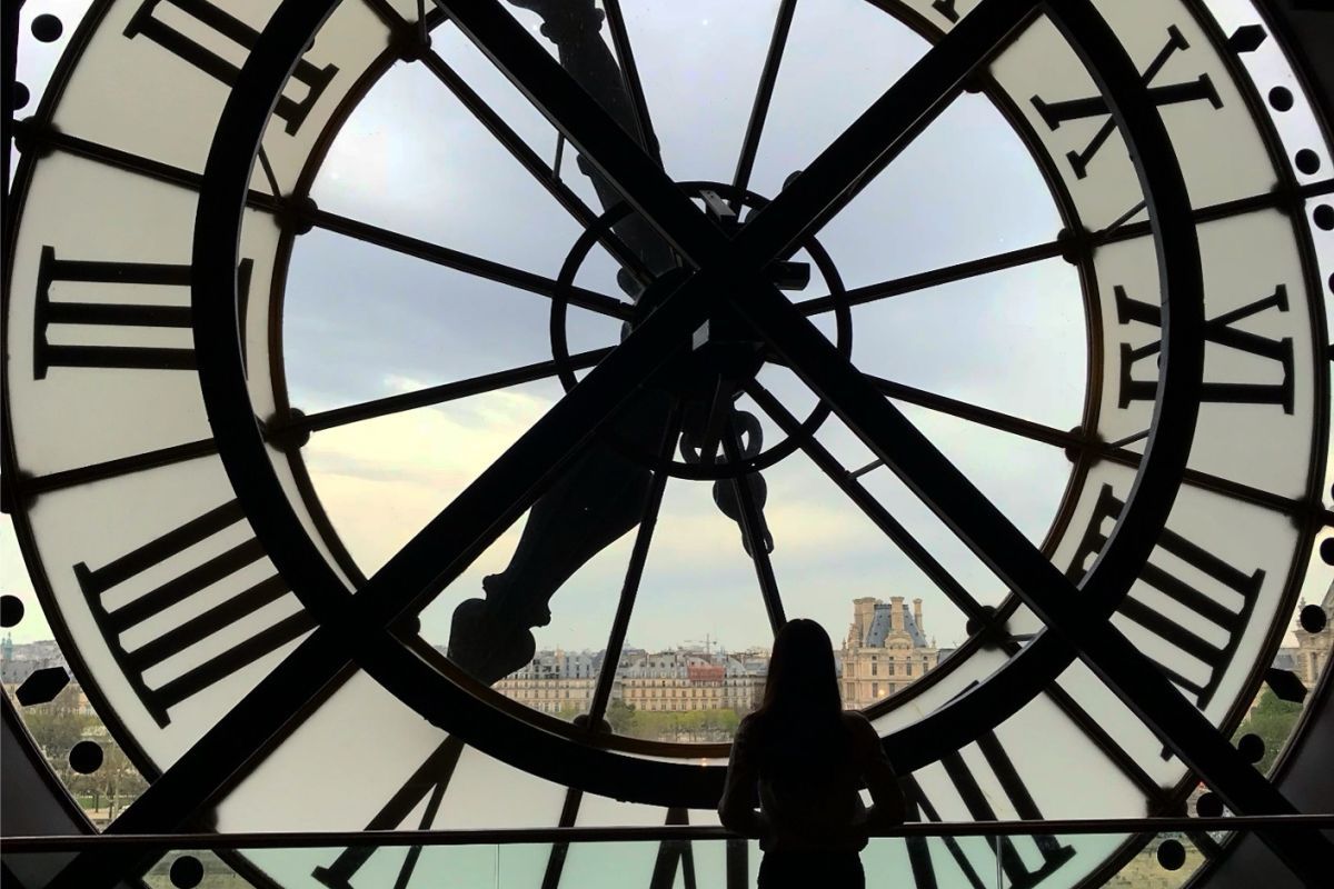 student stands behind clockface looking at european buildings