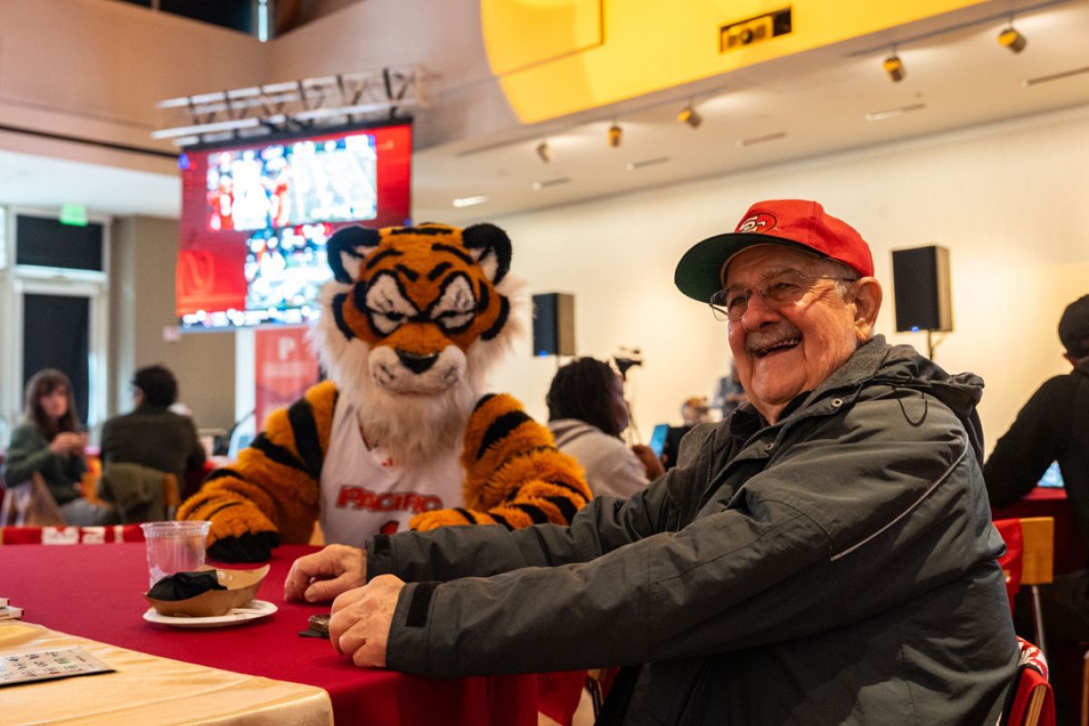 powercat sits with an older man wearing a 49ers hat during the watch party