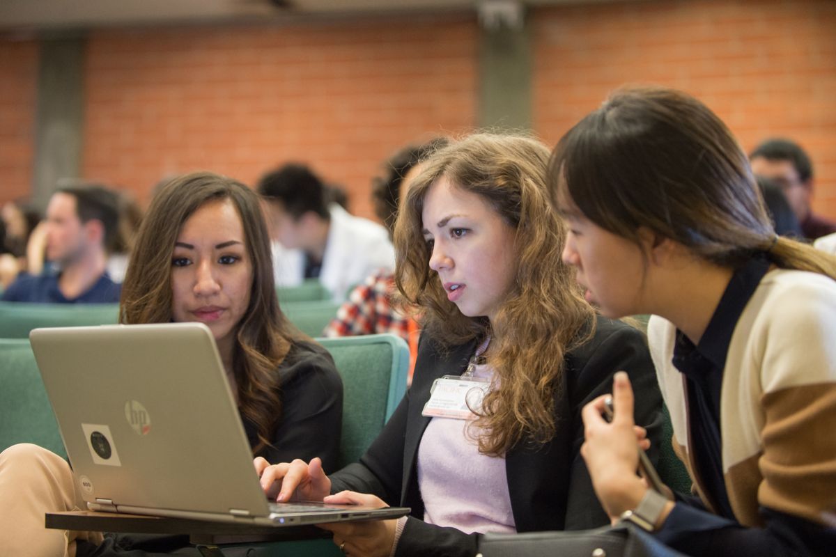 Photos shows three PA students at UOP gathered around a laptop in a lecture hall. 