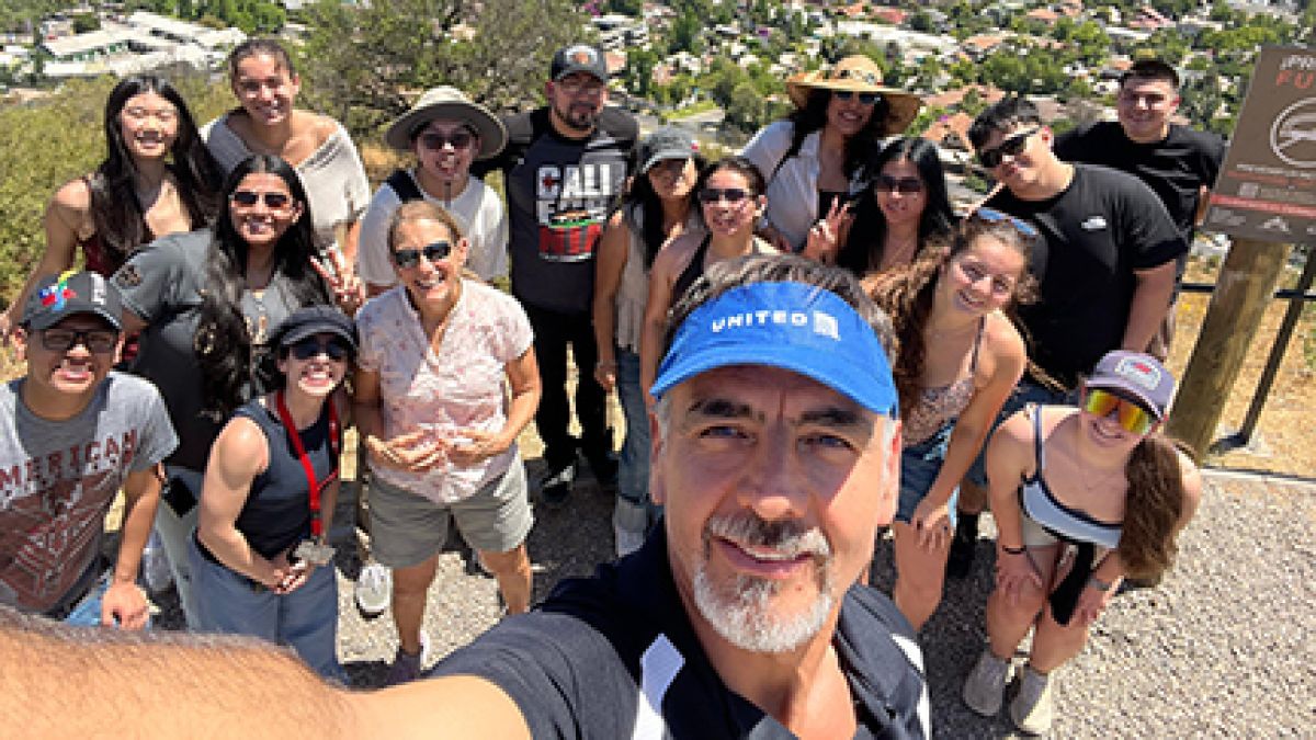 A group of students pose on a mountain top with the city below