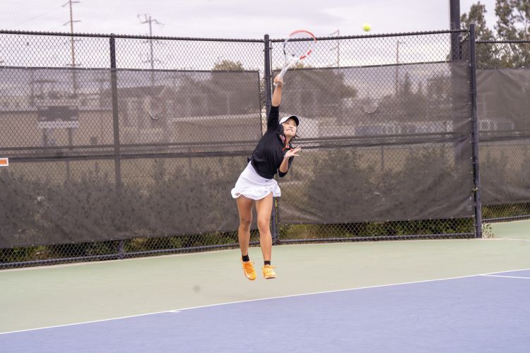A student serves a ball on a tennis court