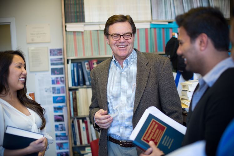A professor laughs with a few students in an office