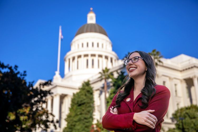A woman in a red suit smiles in front of the California Capitol State Building 