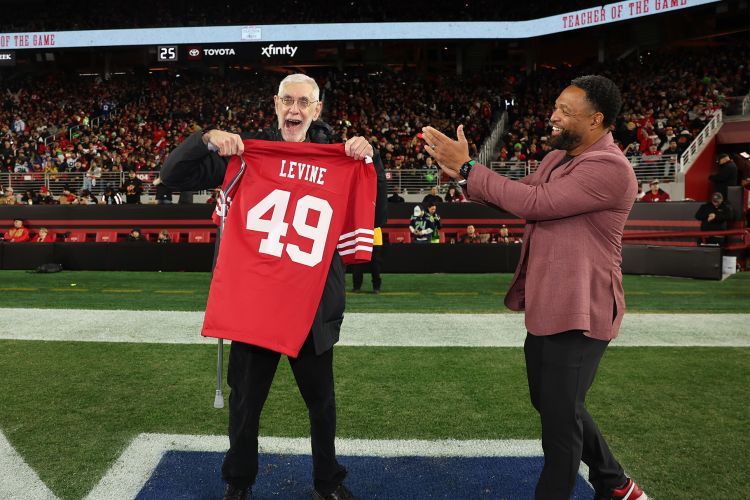 Larry Levine holds up a 49es jersey on the field