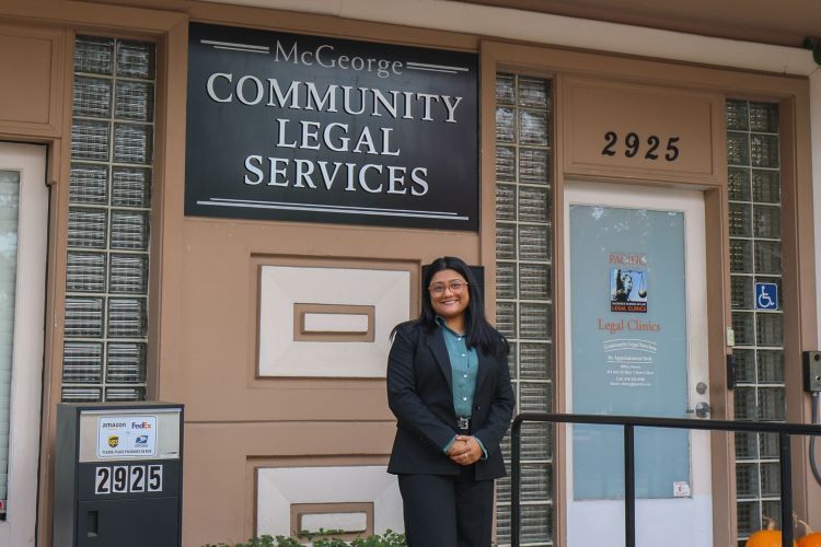A woman wearing a suit poses for a photo outdoors on a campus