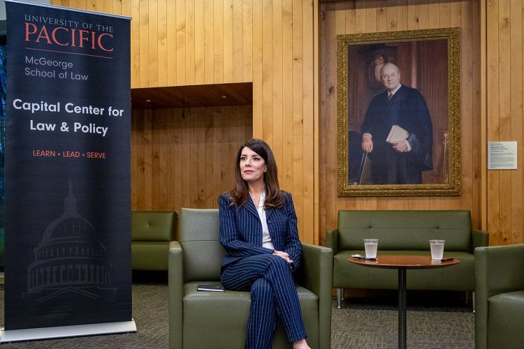 A woman in a dark blue stripped suit sits in a green chair in front of a sign that says "University of the Pacific McGeorge School of Law Capital Center for Law and Policy."