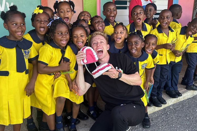 male dental student holding large plastic jaw for teaching the group of children posed with him
