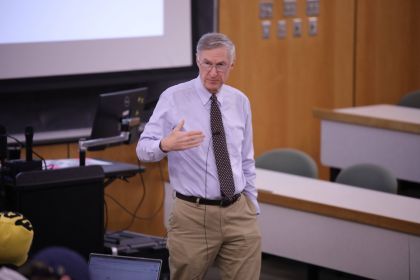 Professor in collared shirt stands and speaks in a classroom setting.