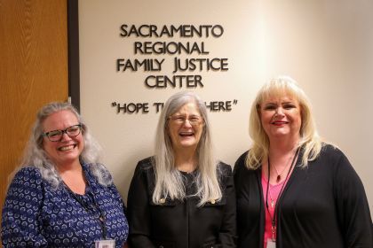 Three women stand in front of a sign that says "Sacramento Regional Family Justice Center.".