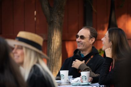 A parent in sunglasses and a black jacket smiles at Homecoming and Family Weekend.