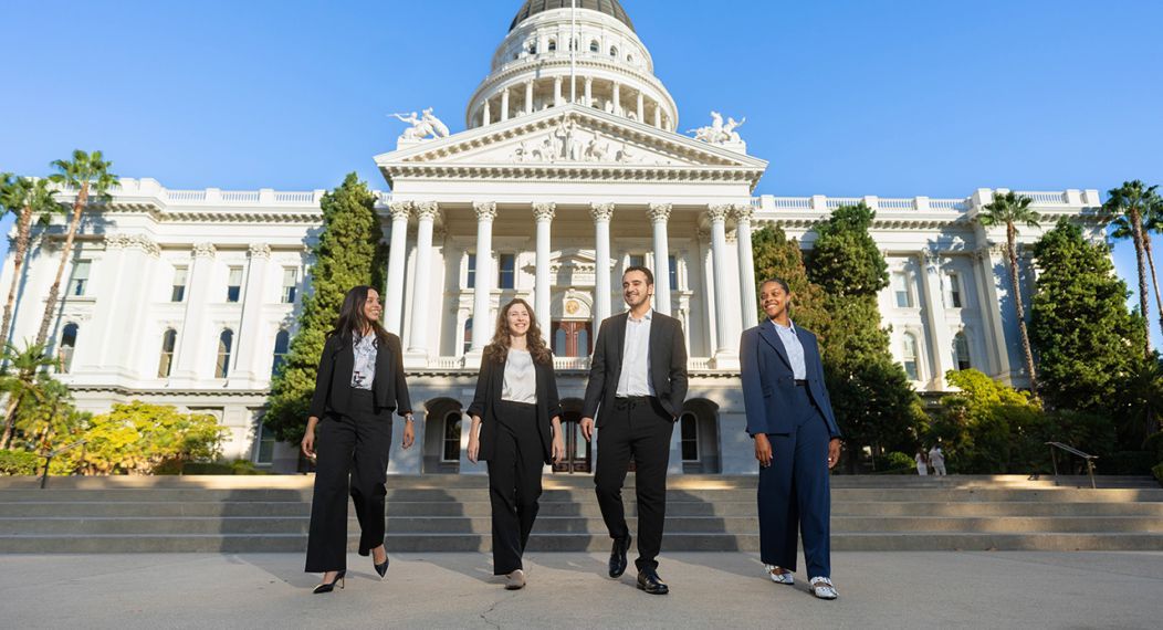 Four individuals walking in business attire in front of the Sacramento Capitol building. 