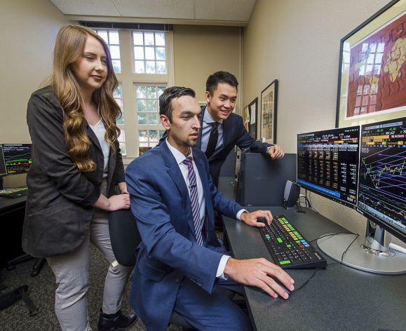 students looking at a computer screen examining stock prices