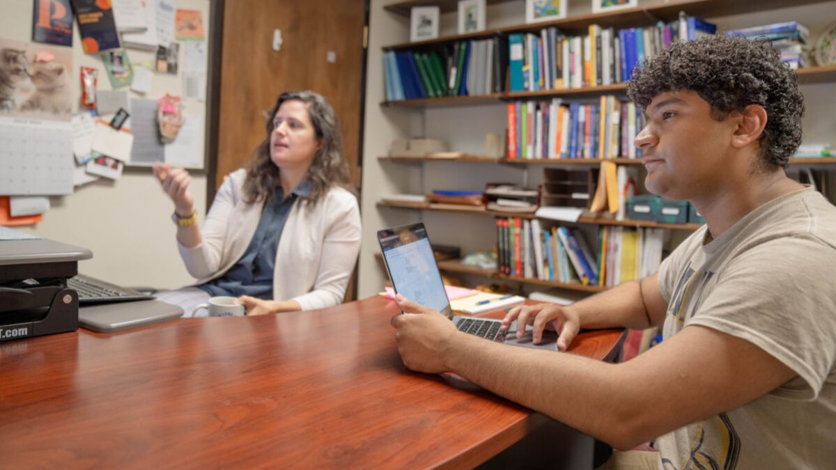 A professor and a student seated at a table in an office
