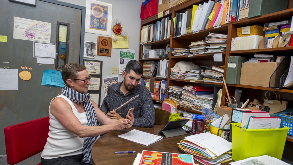 a student and professor sit at a table in an office with many books