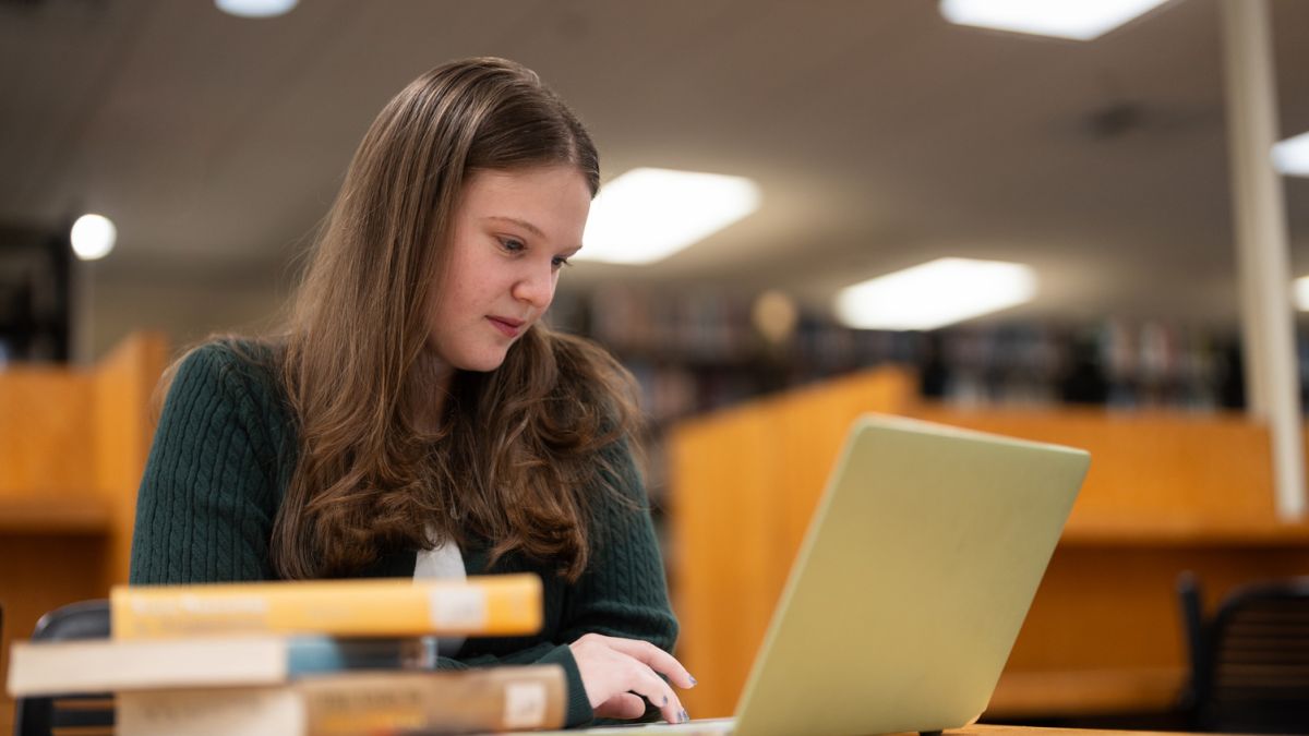 a student sits at a table with books and a laptop